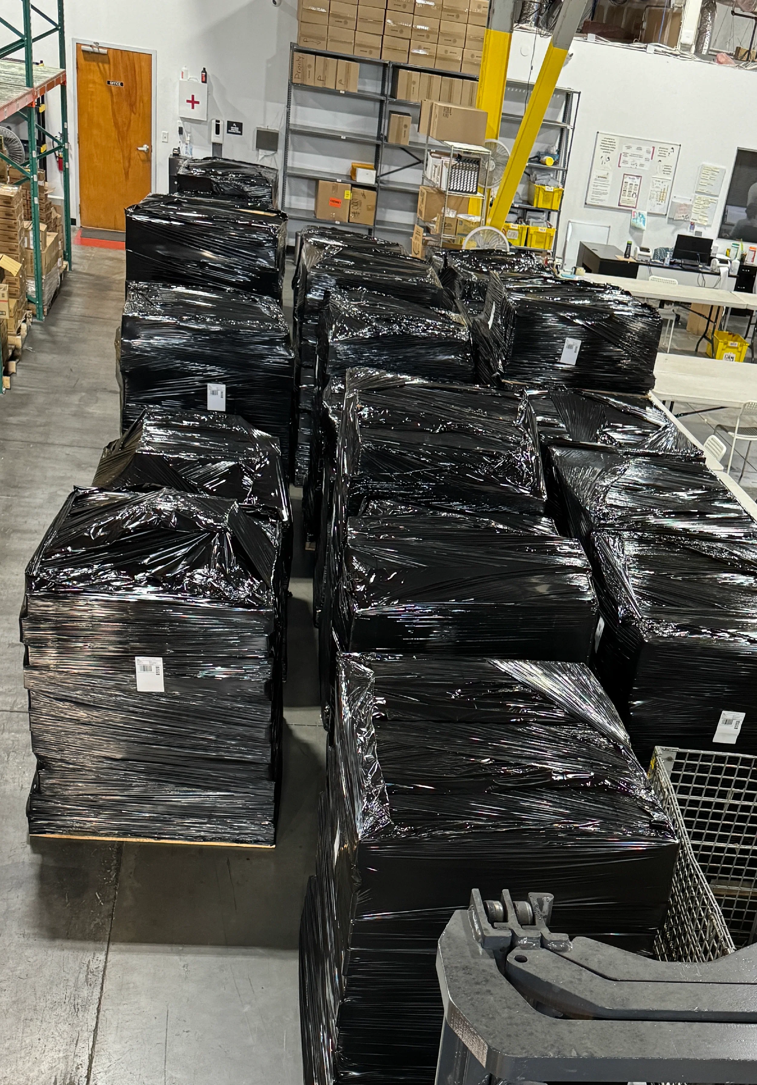 Pilas de palets envueltos en plástico negro en un almacén.