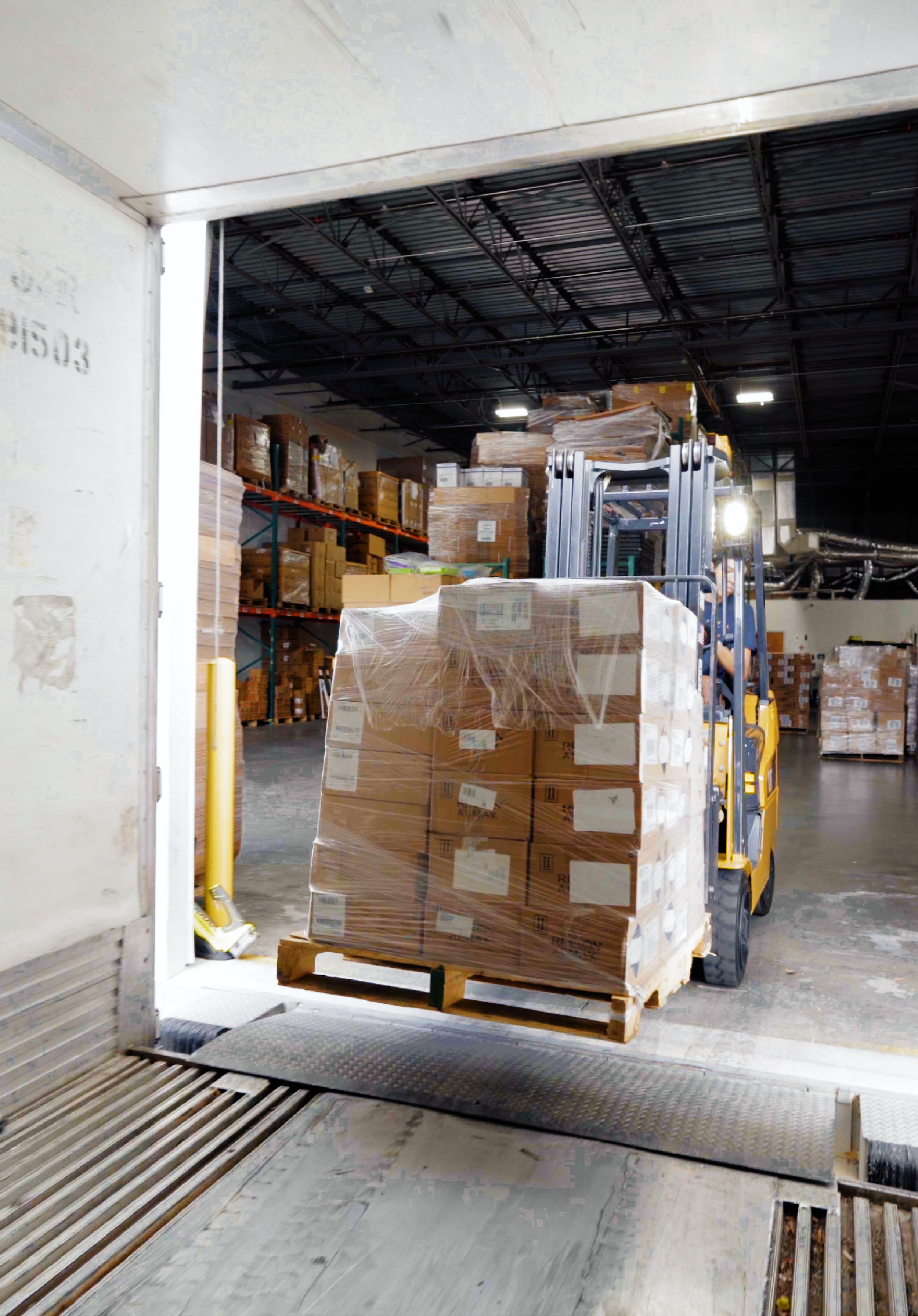 Un montacargas moviendo un palet cargado de cajas dentro de un almacén, con estanterías de cajas empaquetadas al fondo.