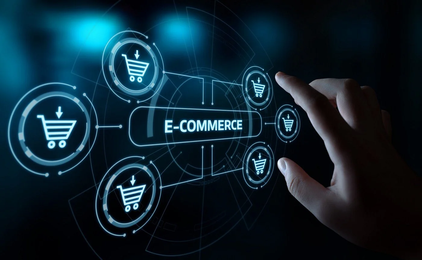 Un gráfico digital que muestra una mano señalando un ícono de carrito de compras virtual conectado a la palabra 'E-COMMERCE' con múltiples íconos similares alrededor.