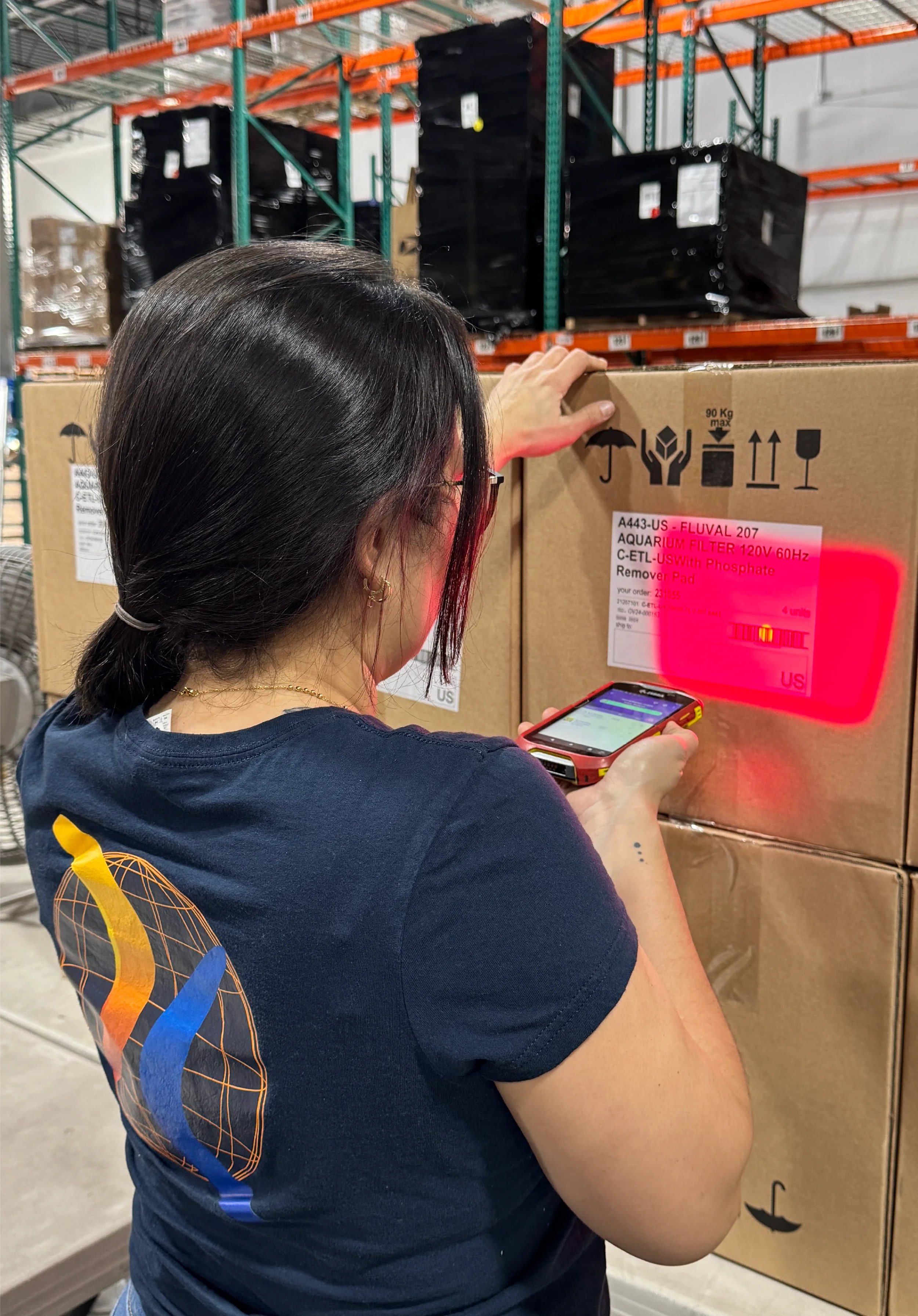 Una mujer escaneando una etiqueta de código de barras en una caja de cartón con su teléfono en un almacén.